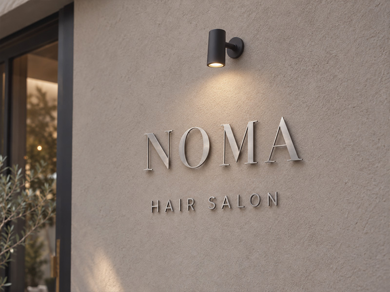 ヘアライン仕上げのシルバーのステンレス切り文字「NOMA HAIR SALON」をグレージュの外壁に配置した製作イメージ